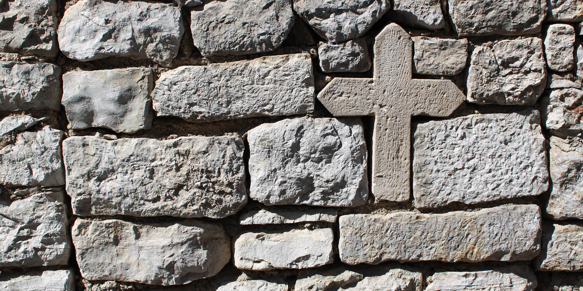 Das Bild zeigt eine Mauer, in der ein Stein wie ein Kreuz geformt ist Mauer